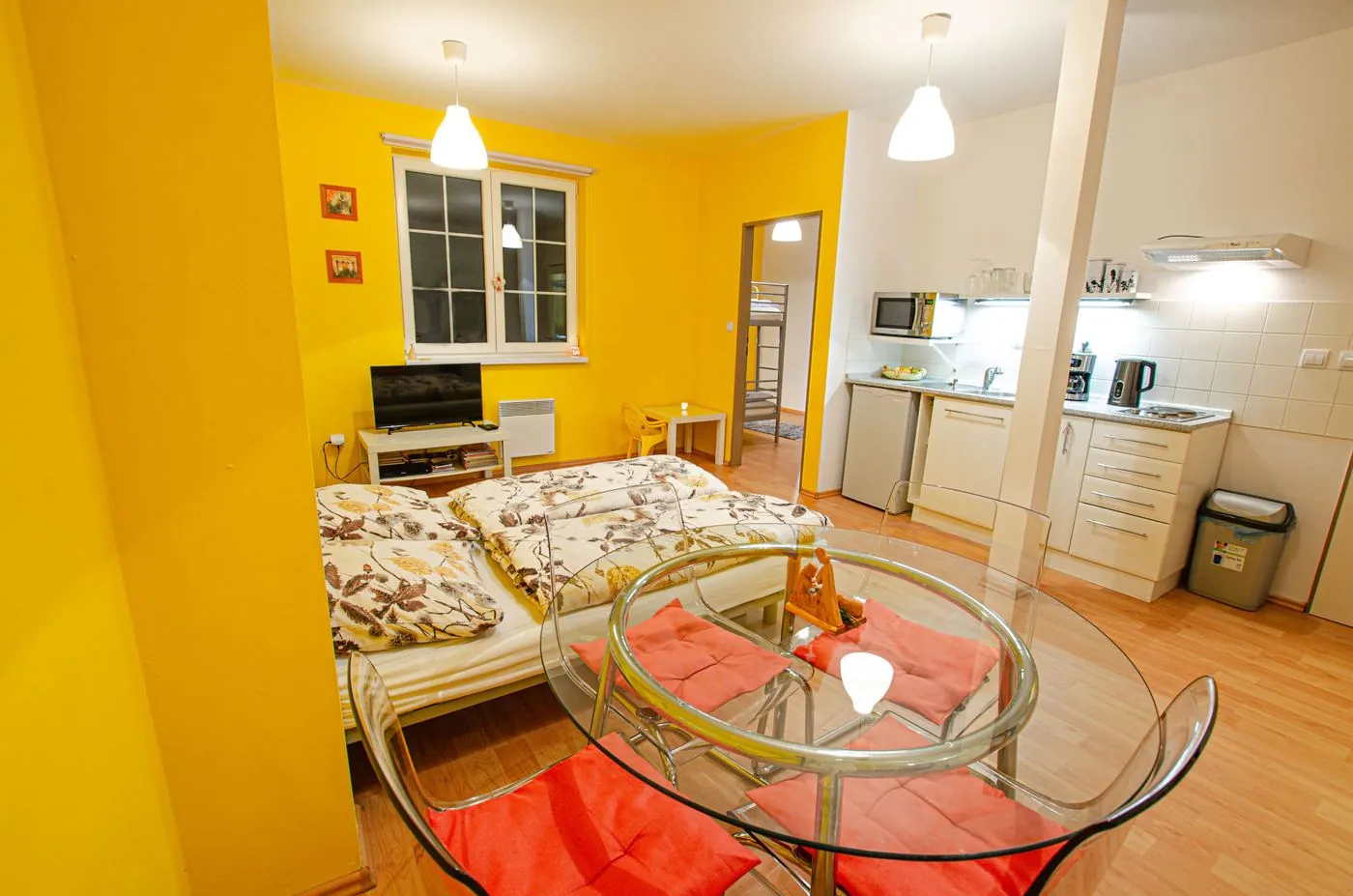 Obývací část apartmánu se skleněným stolem, postelí a kuchyňkou
